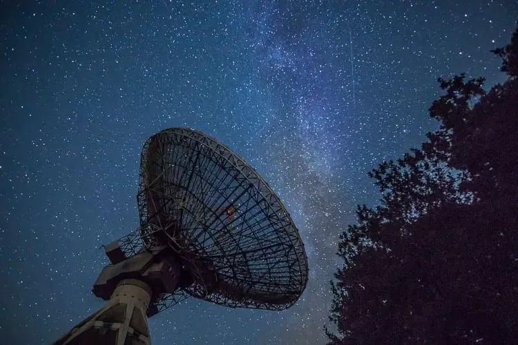 Satellite dish pointing to a sky full of stars.